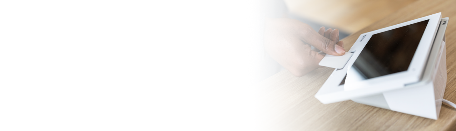 A woman in professional attire holds her smartphone over a credit card processing unit.